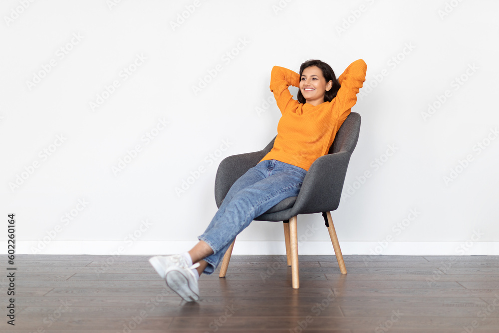 Positive young eastern woman relaxing in armchair at home