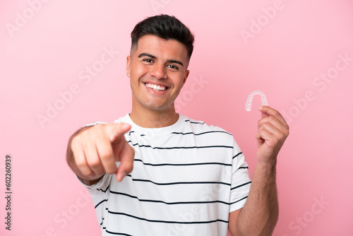 Young caucasian man holding invisaling isolated on pink background points finger at you with a confident expression photo