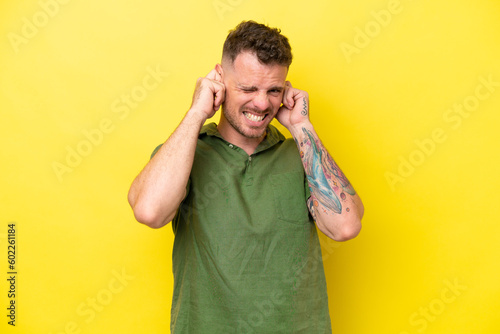 Young caucasian handsome man isolated on yellow background frustrated and covering ears