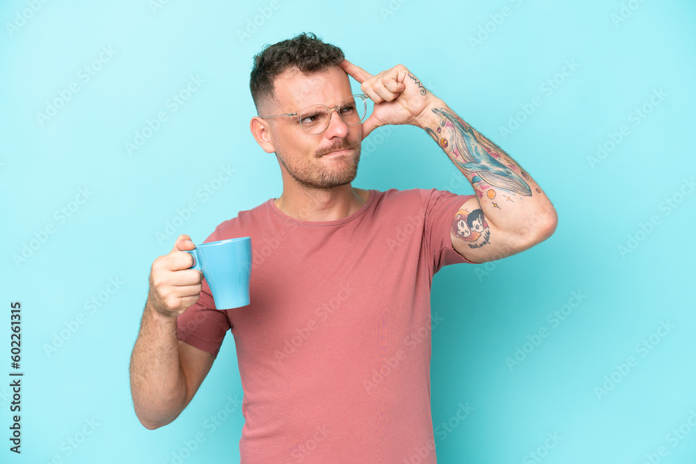 Young caucasian man holding cup of coffee isolated on blue background having doubts and with confuse face expression Young caucasian man holding cup of coffee isolated on blue background having doubts and with confuse face expression