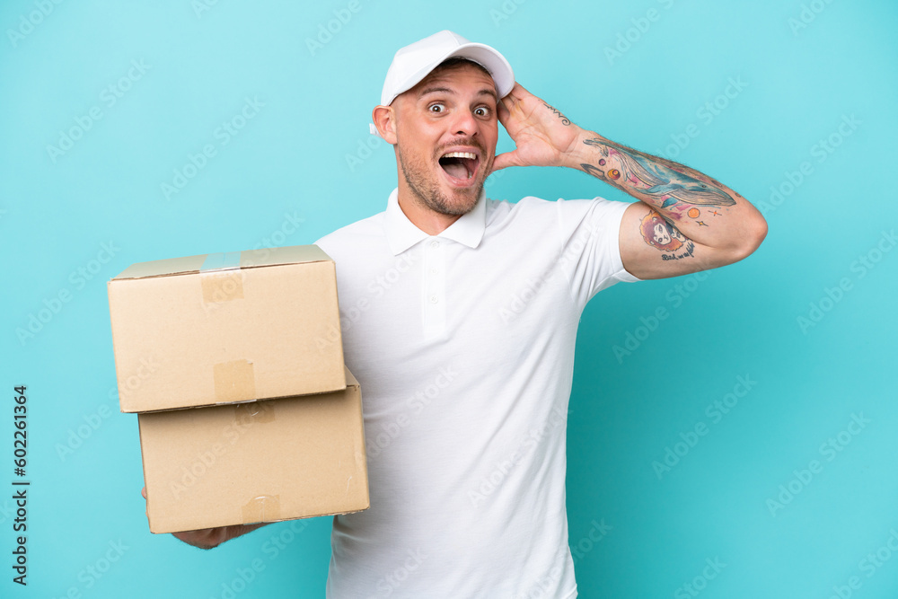 Delivery caucasian man isolated on blue background with surprise expression Delivery caucasian man isolated on blue background with surprise expression
