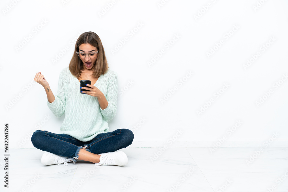 Young caucasian woman sitting on the floor isolated on white background surprised and sending a message Young caucasian woman sitting on the floor isolated on white background surprised and sending a message