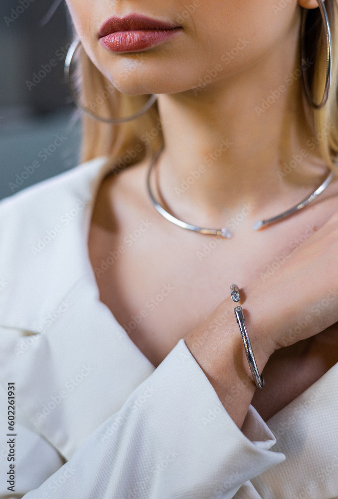 Model showcases a stunning luxurious diamond bracelet on her wrist in the jewelry boutique. The girl is adorned with gold earrings and a necklace, attractive female face, lips, eyes. Successful woman.