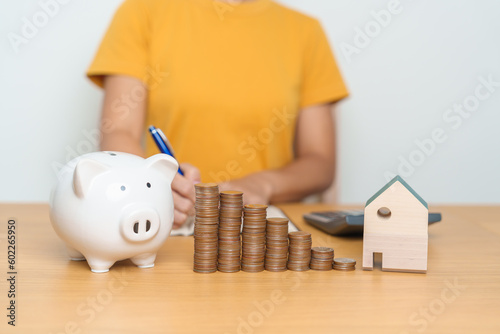 Money Saving, Property investment, House Mortgage and Real Estate Financial concepts. woman with coins stack piggy bank and Home model, Money stack Counting arrangement for deposit and Tax