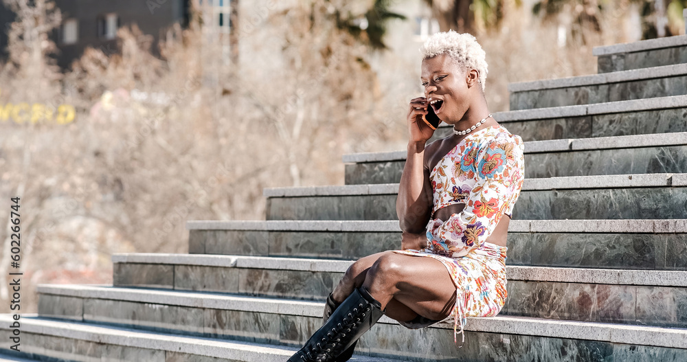 African young transgender woman talking on the phone and smiling on a sunny day.