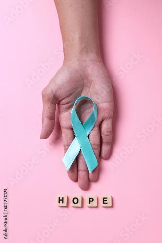 Teal awareness ribbon with hope lettering on cube over pink background. Support to fight cervix cancer. 