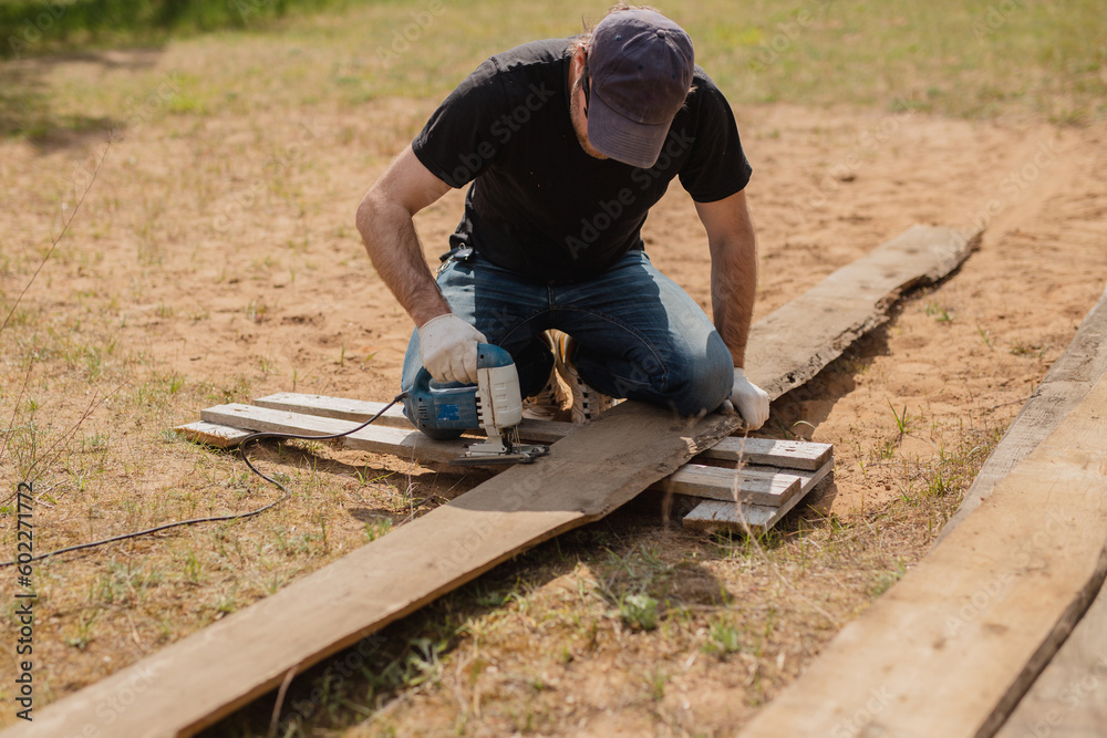 Man builds sections of fence around his yard out of planks - summer home chores in the backyard Man builds sections of fence around his yard out of planks - summer home chores in the backyard