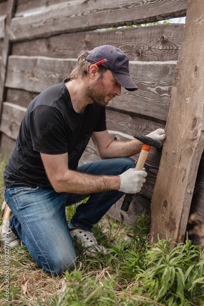 Man builds sections of fence around his yard out of planks - summer home chores in the backyard Man builds sections of fence around his yard out of planks - summer home chores in the backyard