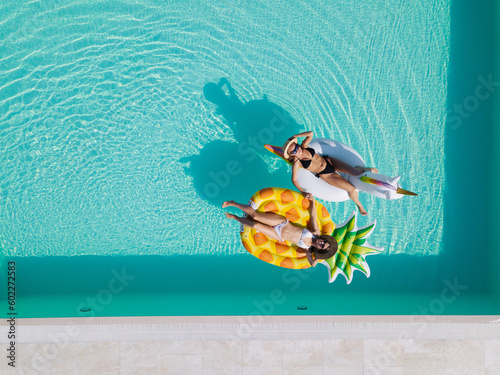 Top view of female friends wearing bikini lying on an inflatable toy in pool. Woman sunbathing on floating pool inflatable toy. © JJ Studio