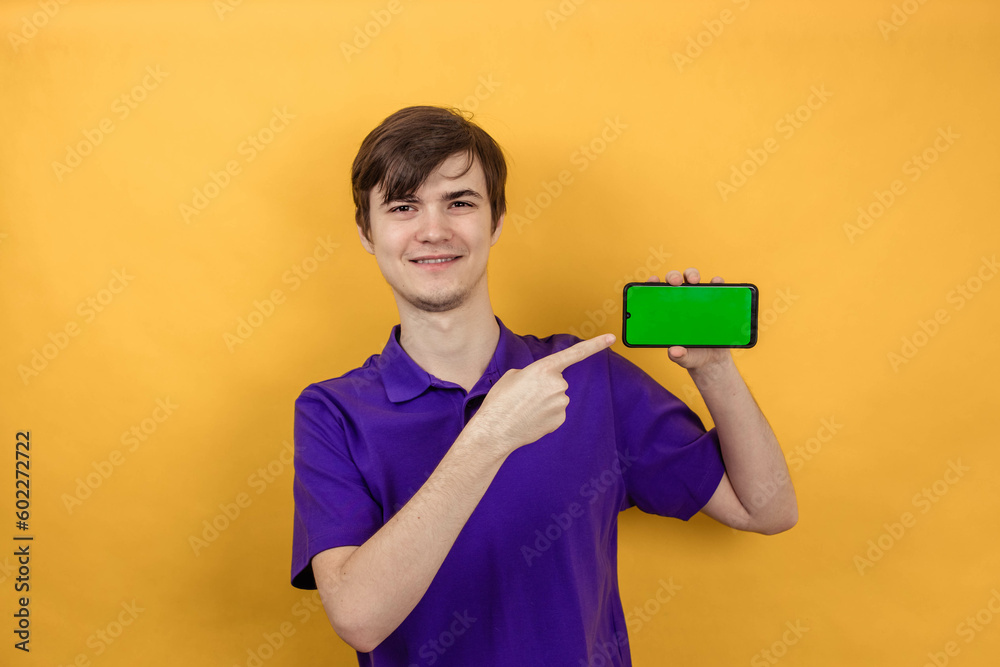 Portrait of a young man points his finger at the smartphone screen on yellow background Portrait of a young man points his finger at the smartphone screen on yellow background