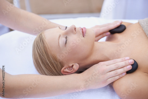Woman getting hot stone massage, hands of masseuse in spa and healing holistic treatment with zen at wellness resort. Rocks on shoulders, peace with therapy, alternative medicine and self care
