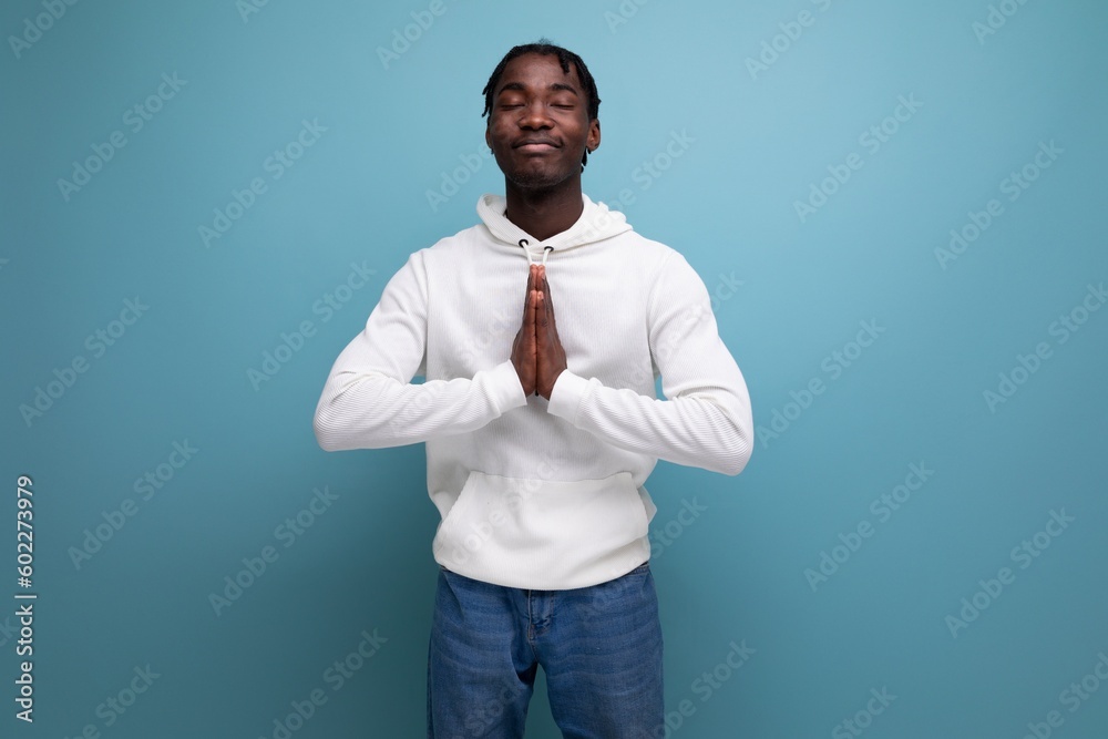 handsome american man in casual clothes praying on blue background