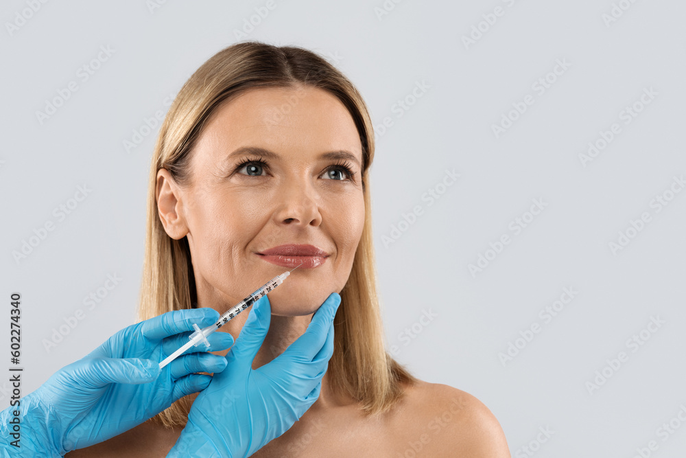 Middle aged woman gets cosmetic injection in lips, copy space Middle aged woman gets cosmetic injection in lips, copy space