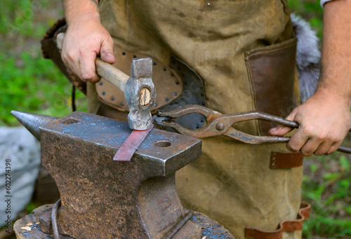 Slika na platnu Blacksmiths hands holding forceps and hammer forging a metal billet, blade of a