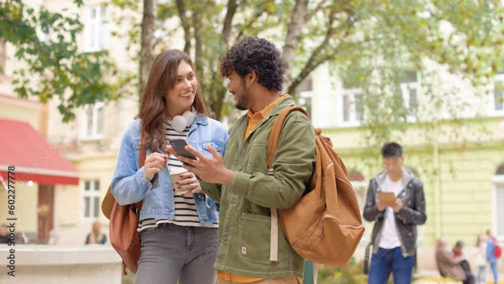 Young happy mixed-race people talking while looking at smartphone screen outdoor. Cheerful handsome man using cellhpone texting surfing internet speaking with pretty female friend on street Young happy mixed-race people talking while looking at smartphone screen outdoor. Cheerful handsome man using cellhpone texting surfing internet speaking with pretty female friend on street