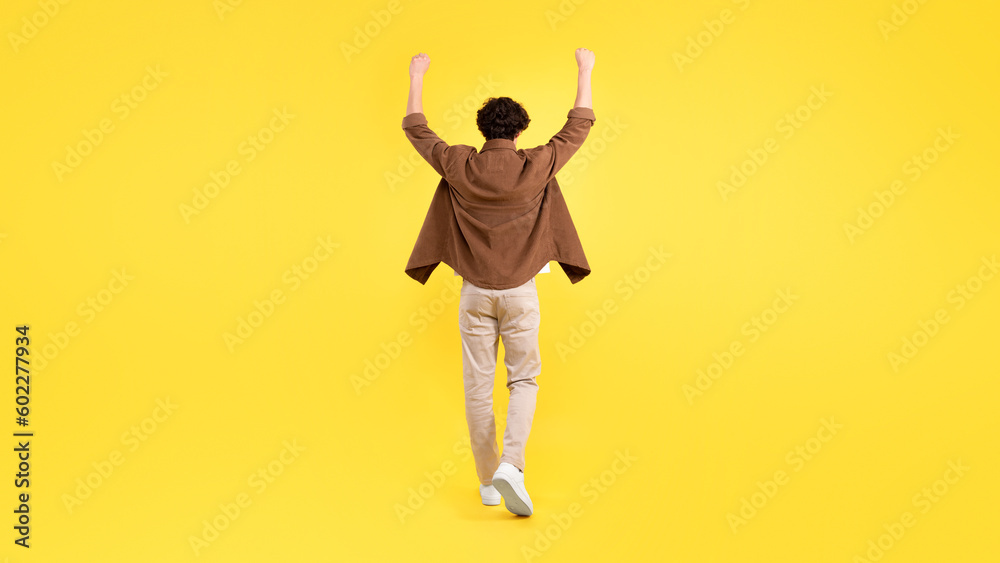 Rear View Of Man Raising Arms Shaking Fists, Yellow Background