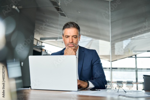 Concerned serious busy professional business man company ceo executive manager wearing suit looking at laptop computer sitting in office thinking of corporate management and financial strategy.