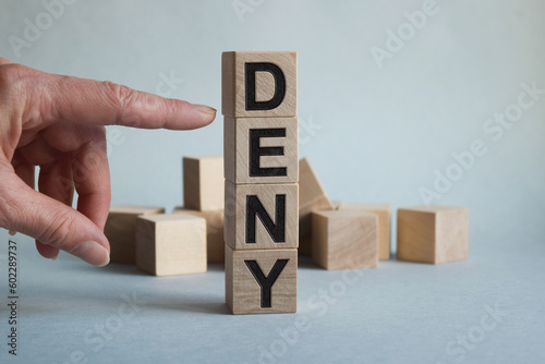 DENY inscription on wooden cubes texture. Close-up of a man's hand points to a cube. The inscription on the financial, business or economic theme.