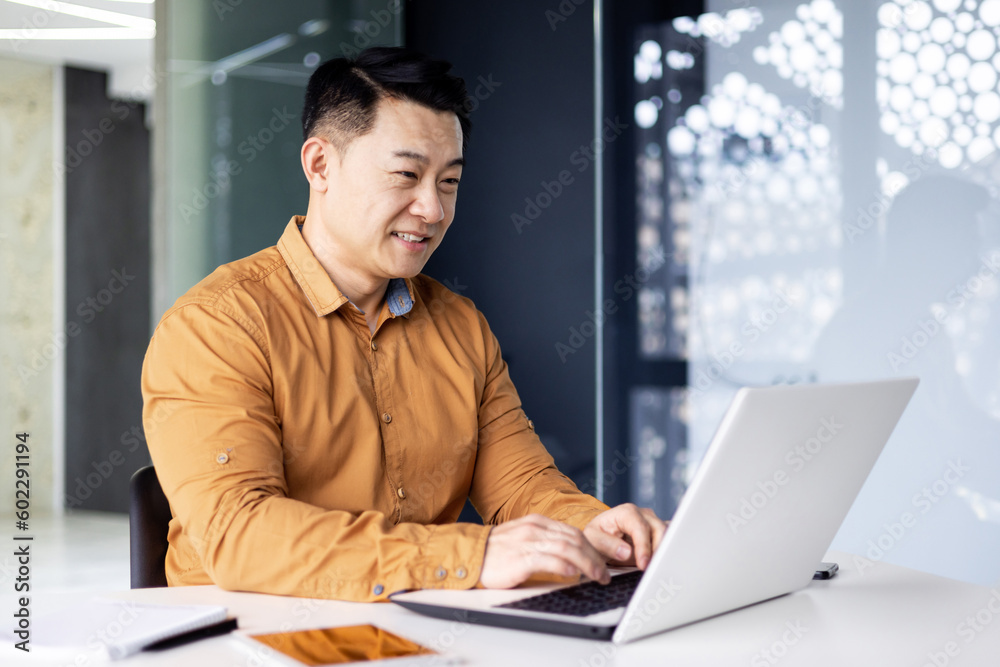 Cheerful and smiling Asian man working inside office, businessman in shirt and glasses using laptop, engineer developer programmer typing code programming software Cheerful and smiling Asian man working inside office, businessman in shirt and glasses using laptop, engineer developer programmer typing code programming software