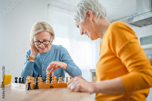 Bild auf Leinwand two women mature senior females sisters play chess board game at home