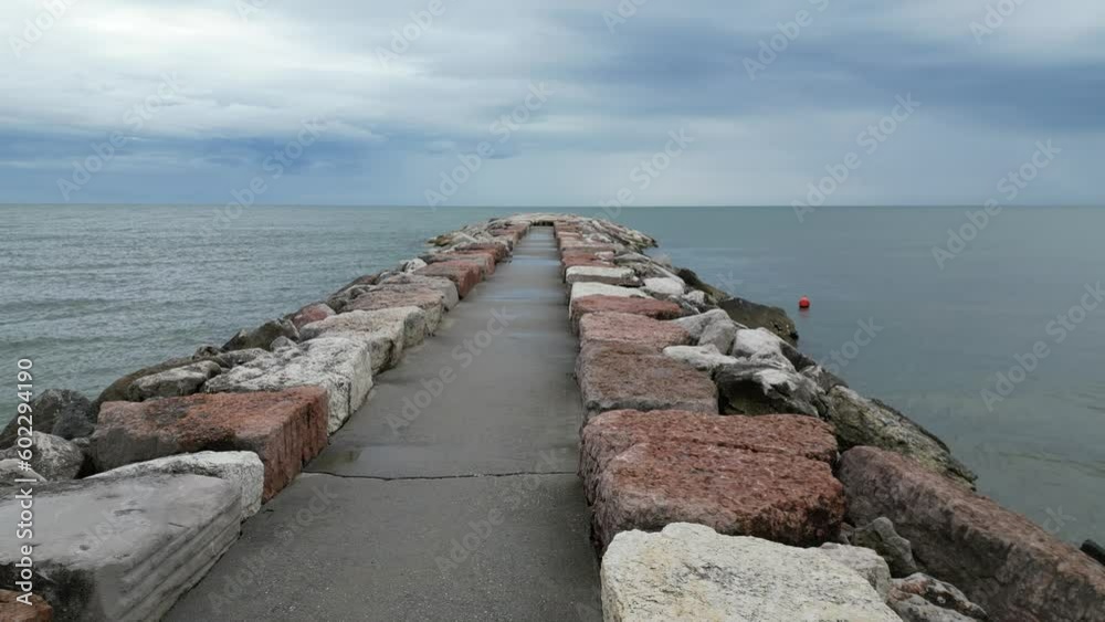 Smooth sea with beach and leaden rocks. Late spring, cloudy skies and rain to come. Italy, Veneto, shore of Eraclea Smooth sea with beach and leaden rocks. Late spring, cloudy skies and rain to come. Italy, Veneto, shore of Eraclea