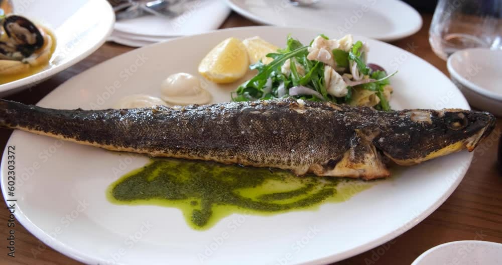 Close up of a well-presented and cooked dish of a whole flathead fish with some vegetable salads on side, ready to eat. Modern Australian seafood cuisine. Real time 4K. Close up of a well-presented and cooked dish of a whole flathead fish with some vegetable salads on side, ready to eat. Modern Australian seafood cuisine. Real time 4K.