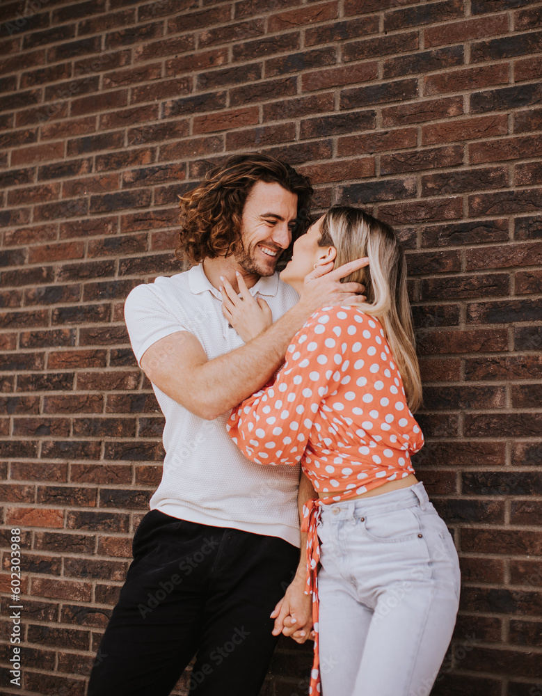 Smiling young couple in love in front of house brick wall
