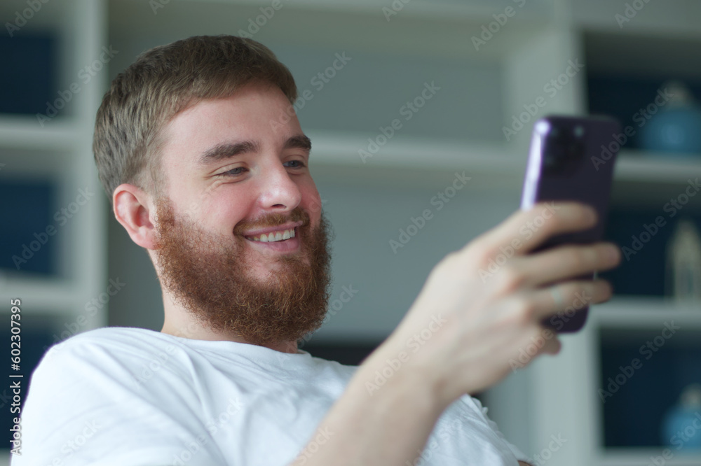Young happy positive adult man relax, on sofa using smartphone for online leisure. People good well rest on lazy day at home or apartment concept. Young happy positive adult man relax, on sofa using smartphone for online leisure. People good well rest on lazy day at home or apartment concept.