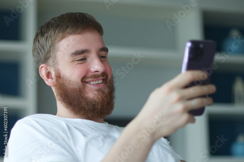 Young happy positive adult man relax, on sofa using smartphone for online leisure. People good well rest on lazy day at home or apartment concept.
