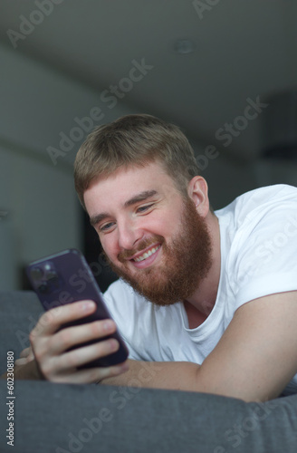 Young happy positive adult man relax, on sofa using smartphone for online leisure. People good well rest on lazy day at home or apartment concept. © Евгений Шемякин