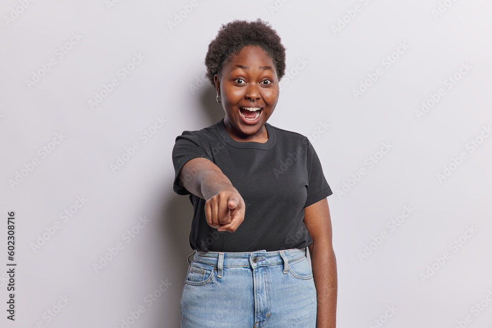 Impressed dark skinned woman points index finger at you picks someting notices something incredible dressed in casual black t shirt and jeans isolated over white backgorund. Wow its incredible Impressed dark skinned woman points index finger at you picks someting notices something incredible dressed in casual black t shirt and jeans isolated over white backgorund. Wow its incredible