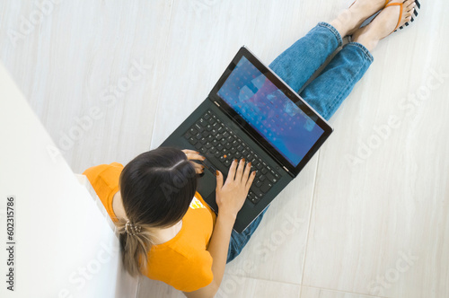 Top view of a young woman holding laptop computer on her lap while sitting at home