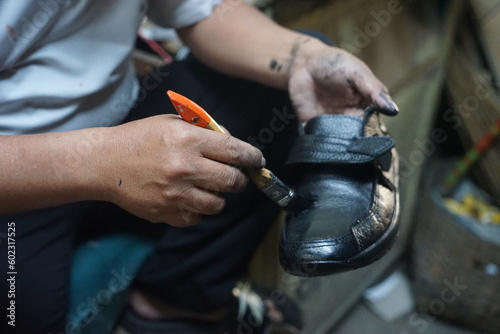 Temanggung, Indonesia - May 10 2023 : An Asian shoe sole repairman is polishing his wares photo
