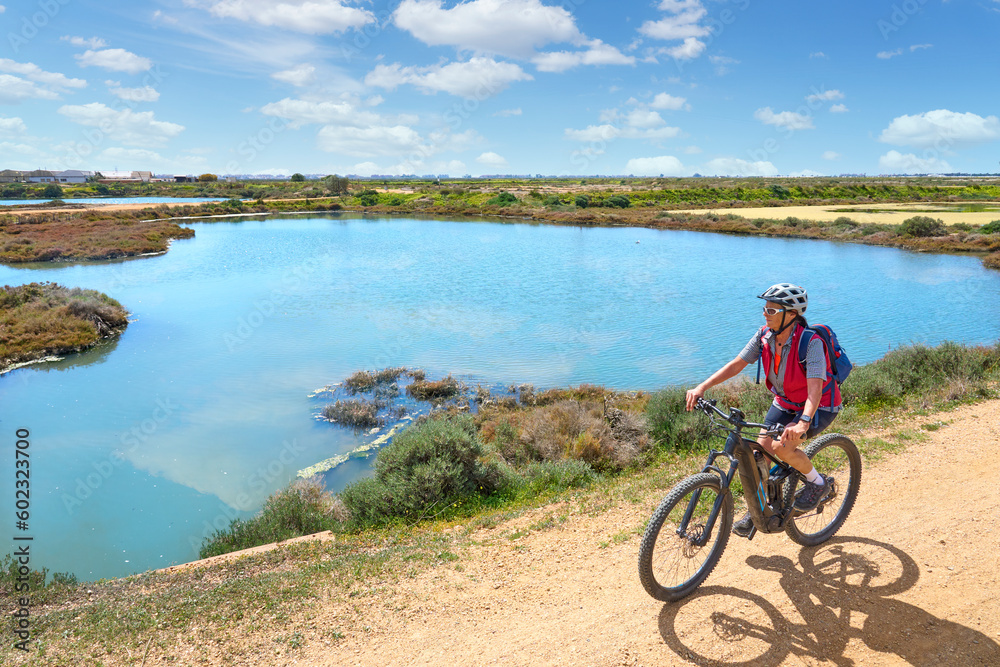 beautiful senior woman cycling with her electric mountain bike on a via verde in the wetlands  of Isla Christina, Andalusia, Spain