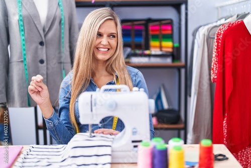 Blonde woman dressmaker designer using sew machine looking away to side with smile on face, natural expression. laughing confident.
