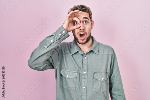 Hispanic man with beard standing over pink background doing ok gesture shocked with surprised face, eye looking through fingers. unbelieving expression. © Krakenimages.com