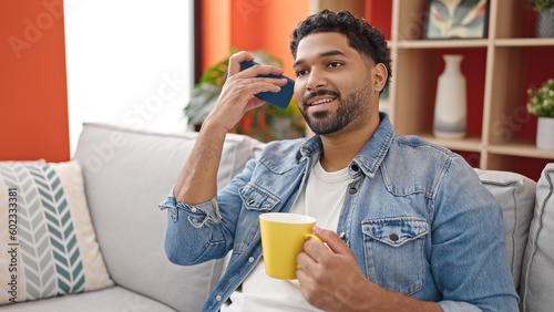 African american man listening voice message by smartphone drinking coffee at home