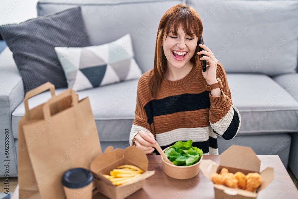 Young woman talking on the smartphone eating take away food at home