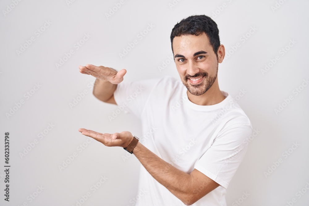 Handsome hispanic man standing over white background gesturing with hands showing big and large size sign, measure symbol. smiling looking at the camera. measuring concept.