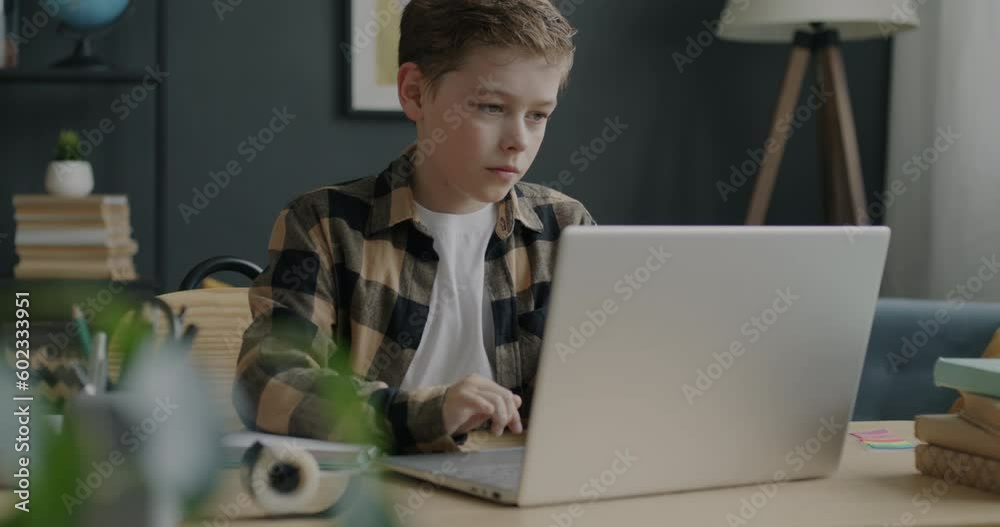 Portrait of pensive child working with laptop computer browsing sitting at desk at home. Modern lifestyle and happy childhood concept.