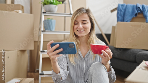 Young blonde woman using smartphone drinking coffee at new home