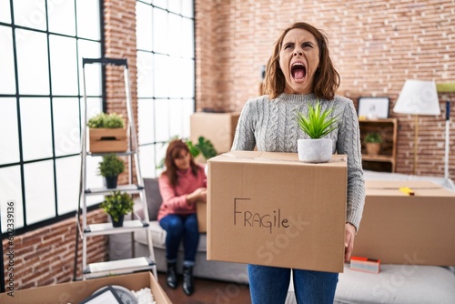 Mother and daughter moving to a new home holding cardboard box angry and mad screaming frustrated and furious, shouting with anger looking up. © Krakenimages.com