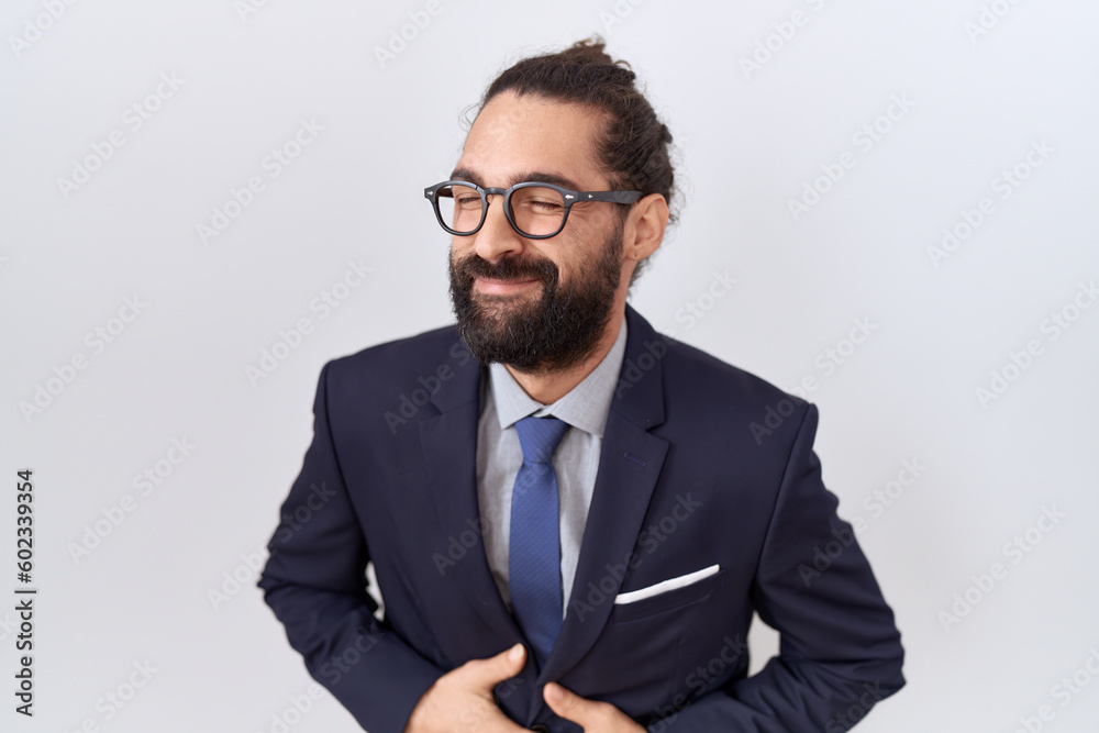 Hispanic man with beard wearing suit and tie with hand on stomach because nausea, painful disease feeling unwell. ache concept. Hispanic man with beard wearing suit and tie with hand on stomach because nausea, painful disease feeling unwell. ache concept.