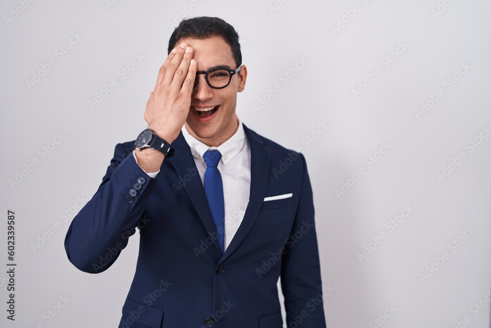 Young hispanic man wearing suit and tie covering one eye with hand, confident smile on face and surprise emotion. Young hispanic man wearing suit and tie covering one eye with hand, confident smile on face and surprise emotion.