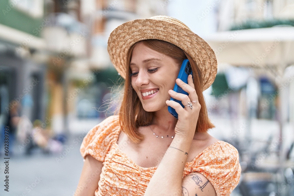 Young redhead woman tourist wearing summer hat talking on smartphone at street