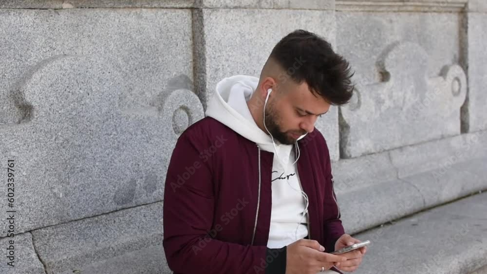 Man listening to music with headphones while typing on his mobile phone