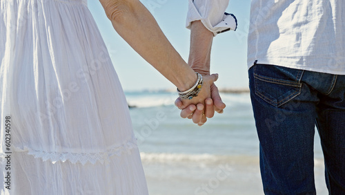 Senior man and woman couple standing with hands together at seaside