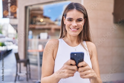 Young beautiful hispanic woman smiling confident using smartphone at coffee shop terrace