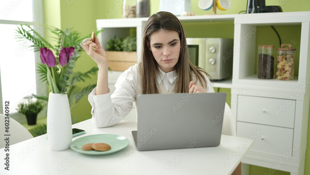 Young beautiful hispanic woman eating cookies using laptop at dinning room Young beautiful hispanic woman eating cookies using laptop at dinning room