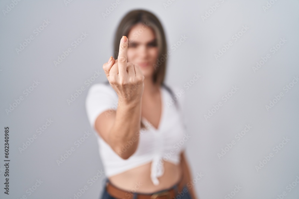 Young beautiful woman wearing casual white t shirt showing middle finger, impolite and rude fuck off expression Young beautiful woman wearing casual white t shirt showing middle finger, impolite and rude fuck off expression